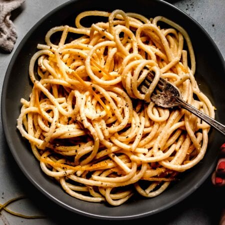 Overhead shot of lemon pasta in bowl next to charred lemon halves.