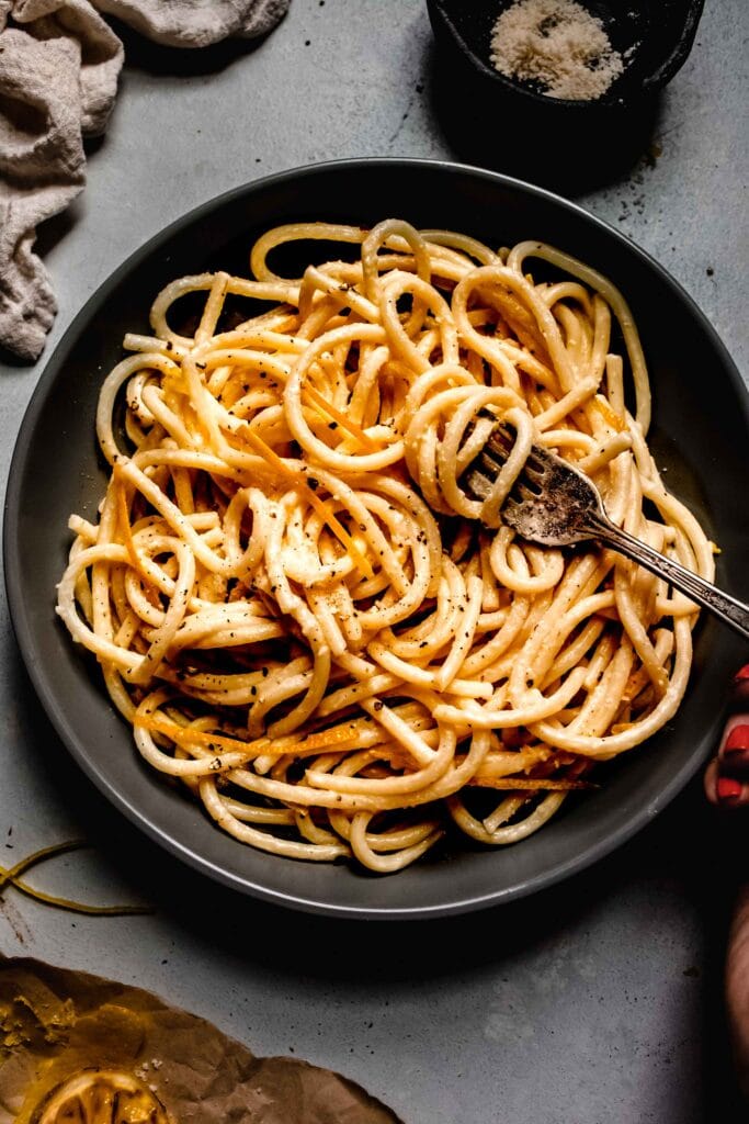 Overhead shot of lemon pasta in bowl next to charred lemon halves.