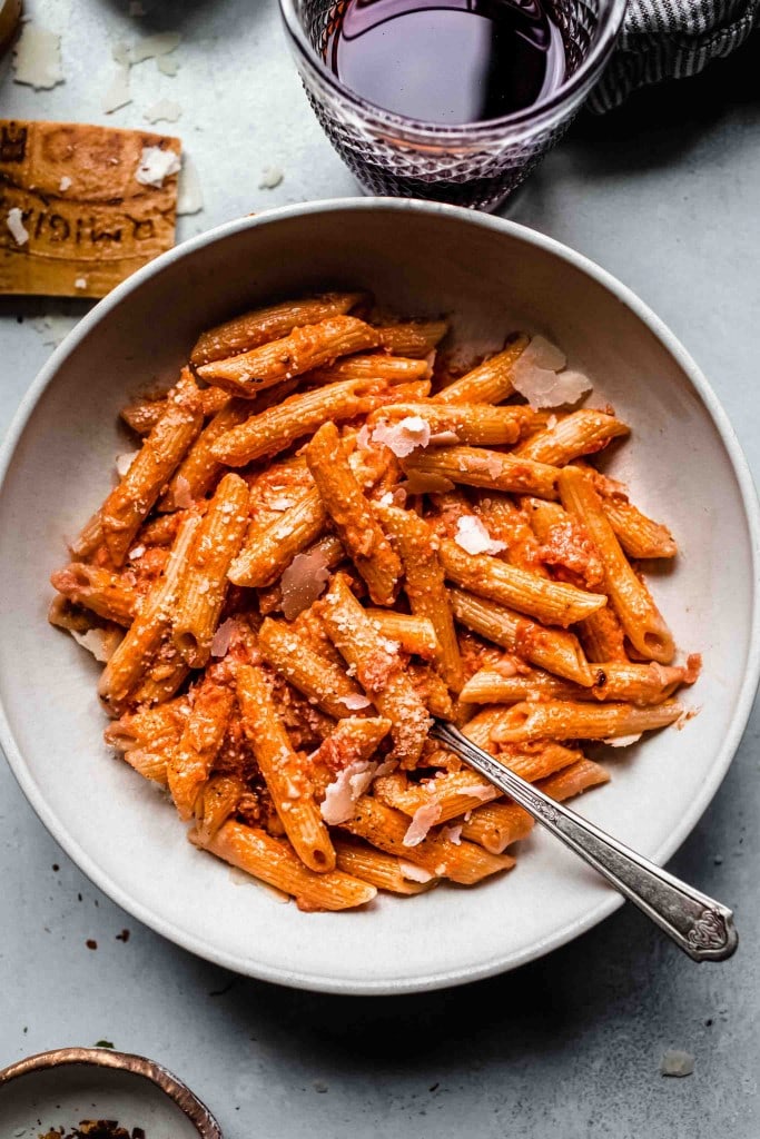 Overhead shot of penne alla vodka in white bowl next to glass of red wine.