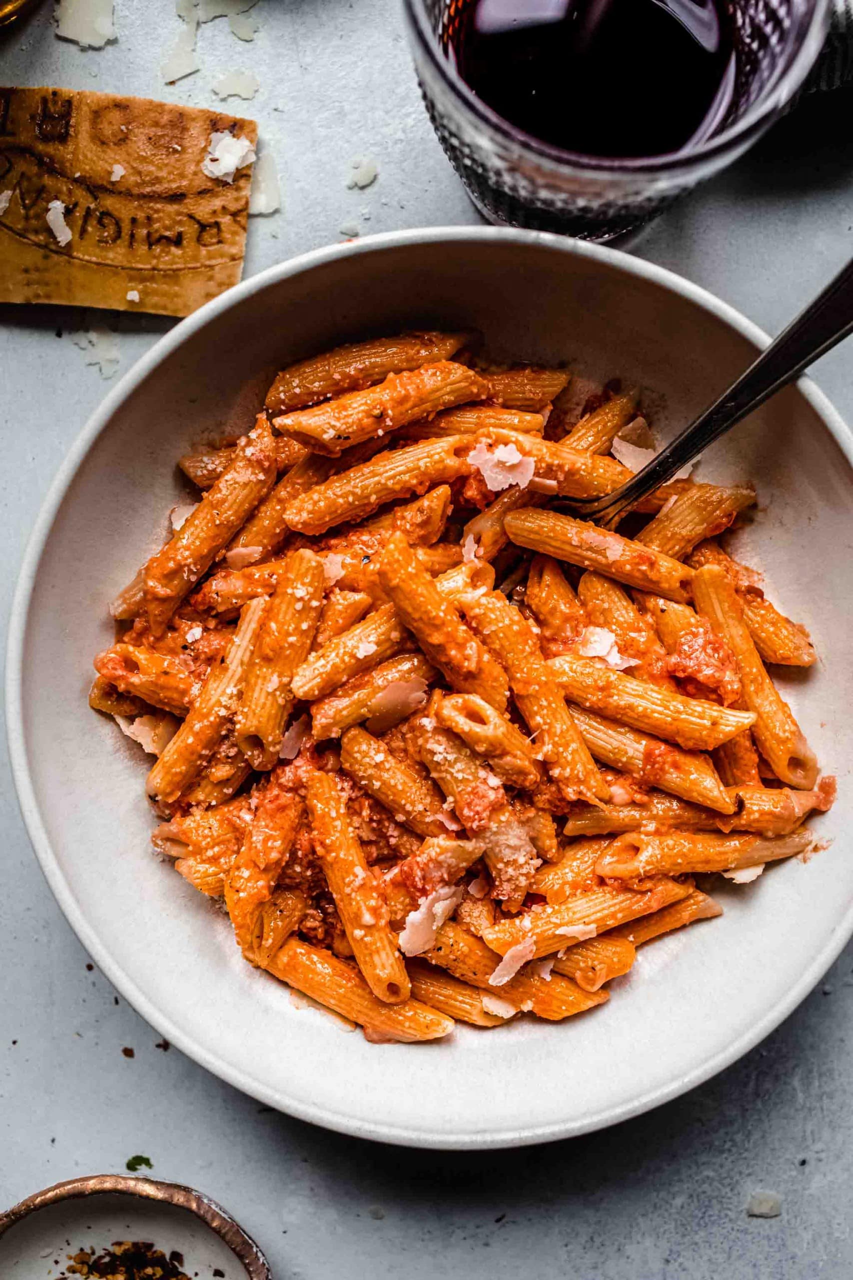 Overhead shot of penne alla vodka in white bowl next to glass of red wine.