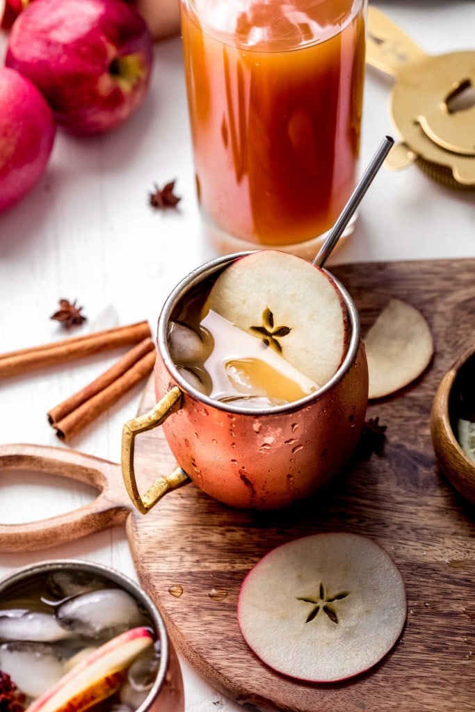 Apple cider moscow mule on serving tray garnished with apple slices and cinnamon stick.