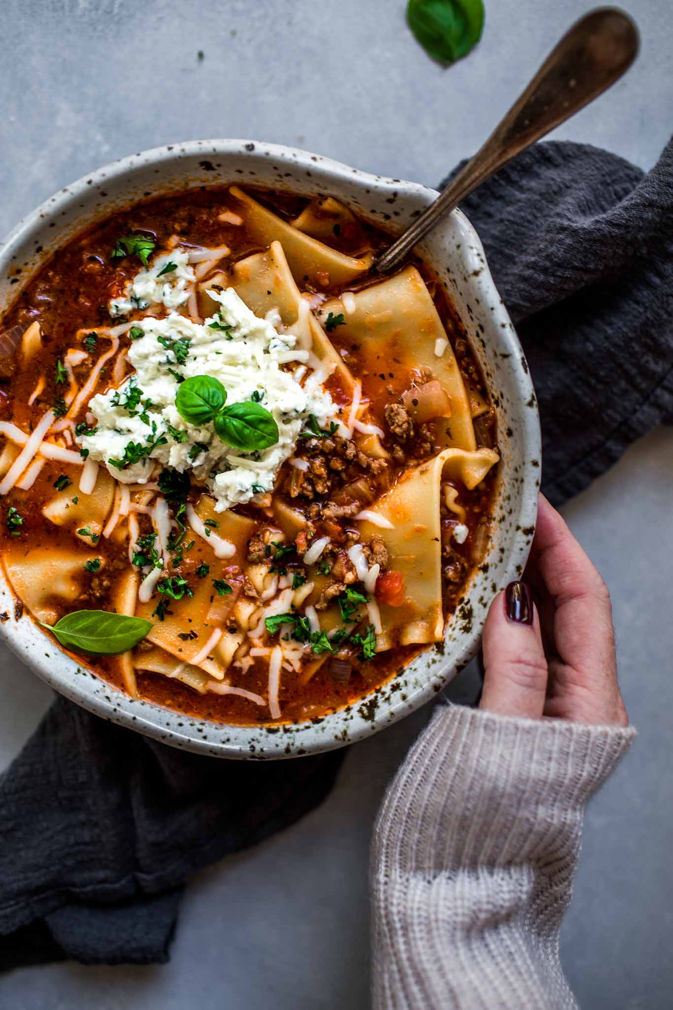 Hand reaching for bowl of lasagna soup.