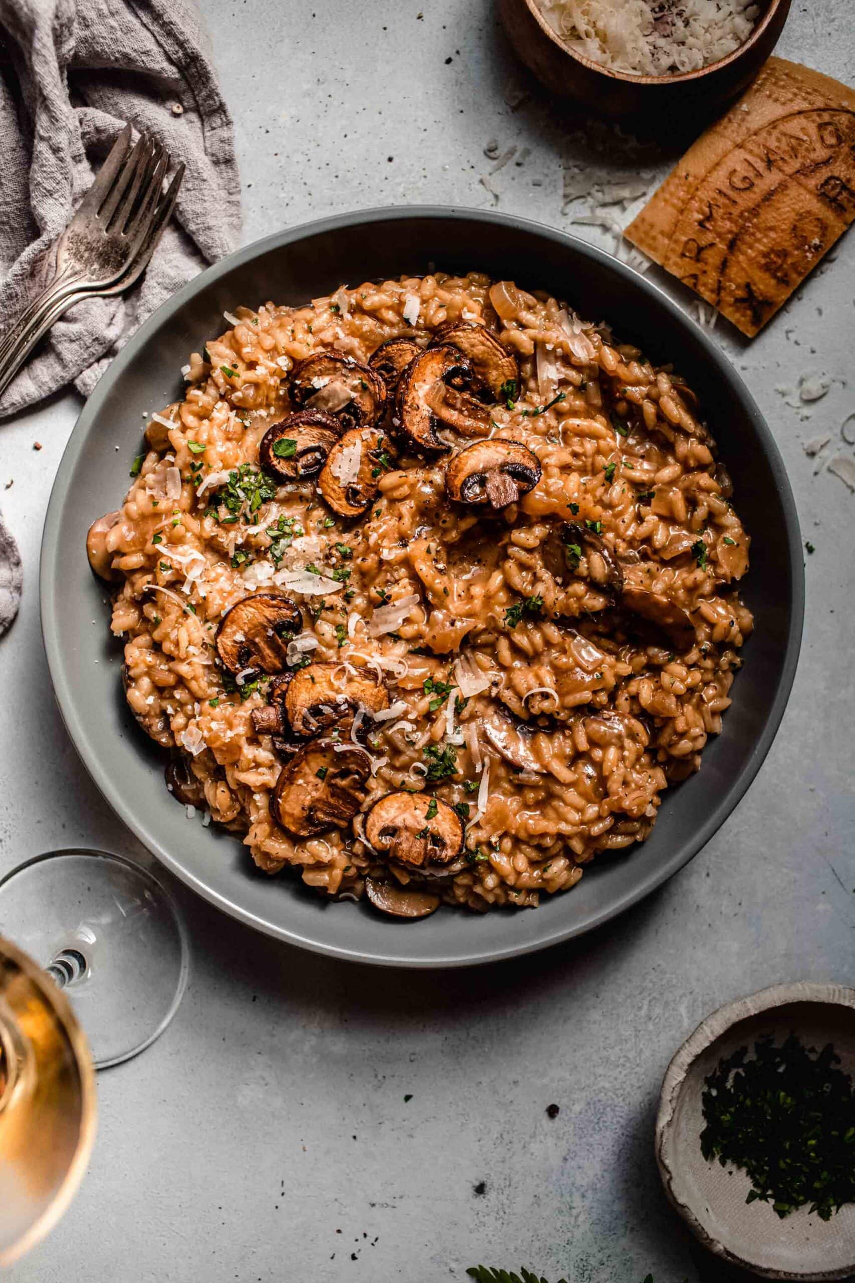 Mushroom risotto in grey bowl next to glass of wine.