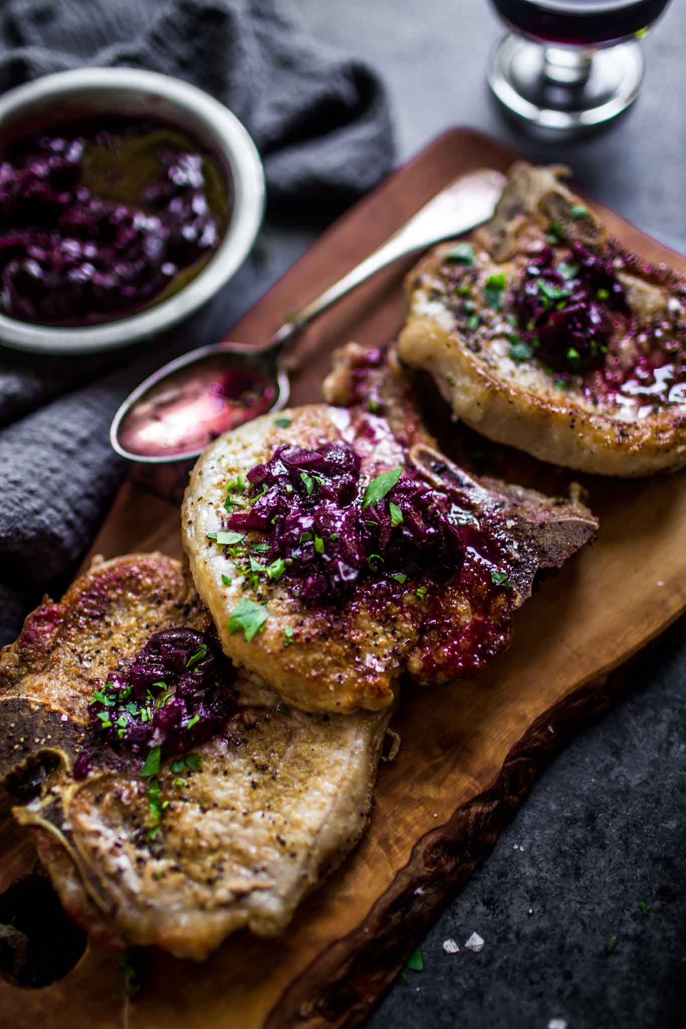 Side view of three pork chops on wood cutting board topped with cherry sauce.