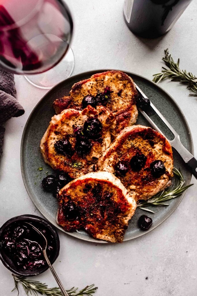 Overhead shot of pork chops next to glass of wine. 