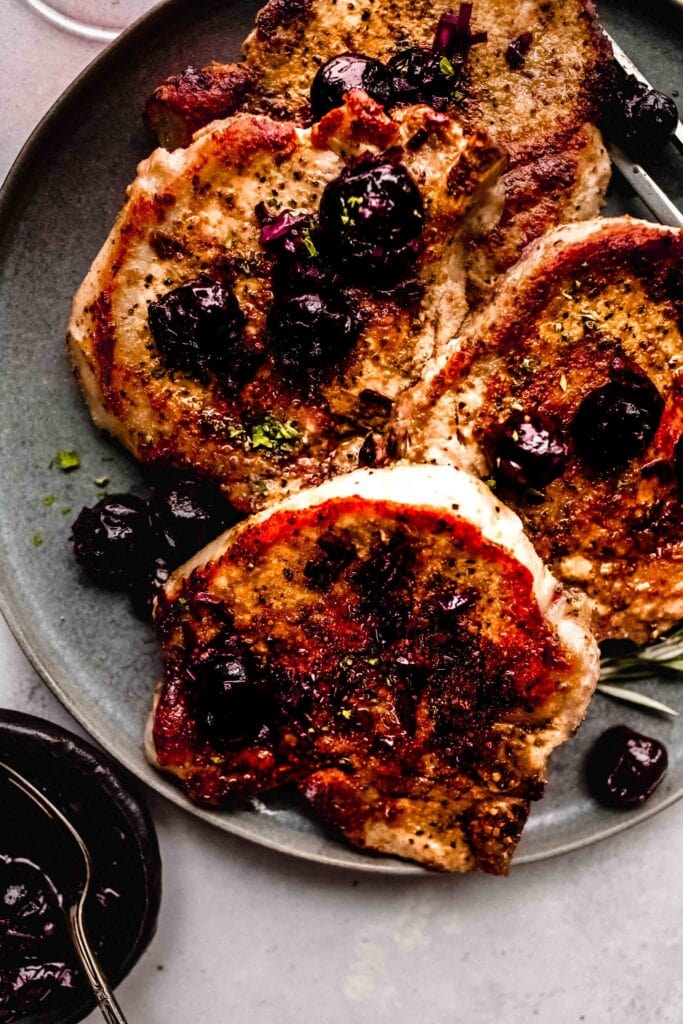 Pork chops on grey plate with rosemary sprigs.