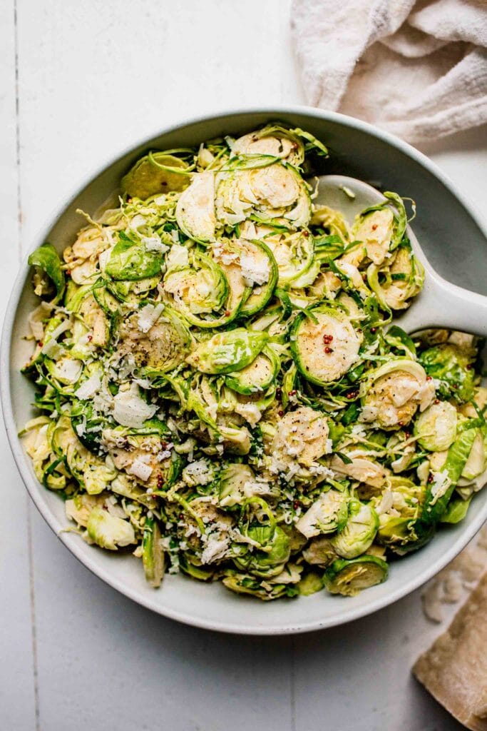 Shaved brussels sprouts salad in large bowl with serving spoon.