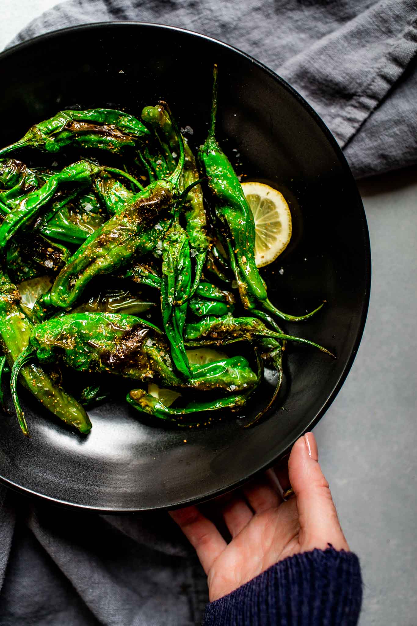 Hand holding plate of blistered shishito peppers. 