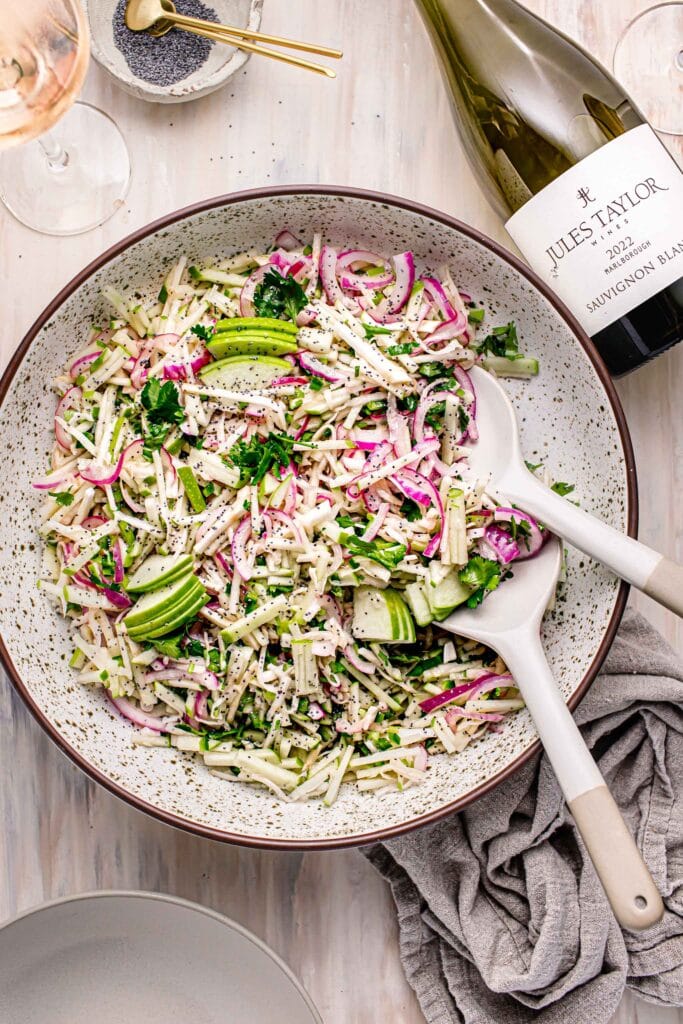 Overhead shot of celery slaw with serving spoons next to bottle of wine.
