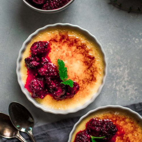 Overhead shot of three ramekins of creme brulee topped with roasted blackberries.