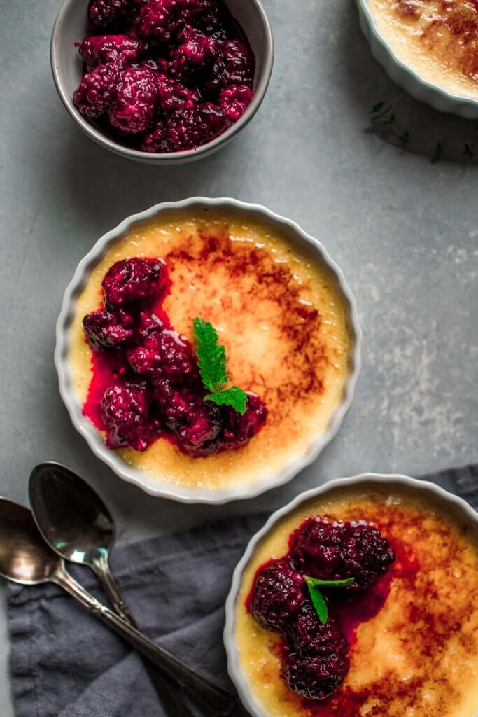Overhead shot of three ramekins of creme brulee topped with roasted blackberries.