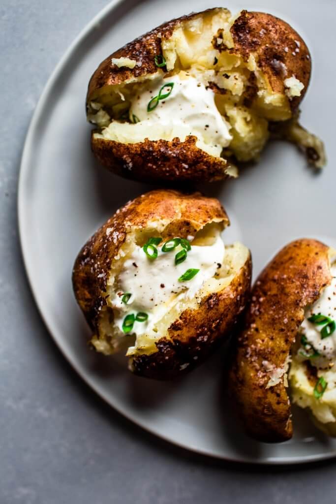 Overhead shot of baked potatoes topped with sour cream and chives.