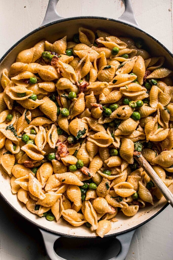 Creamy pasta with peas and bacon in skillet with wooden spoon.