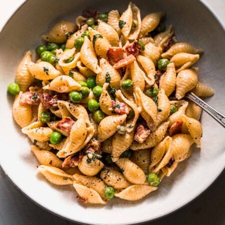 Bowl of pea and bacon pasta on white counter.