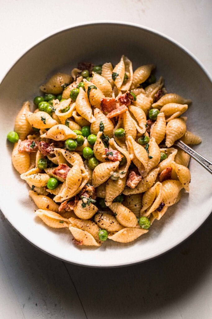 Bowl of pea and bacon pasta on white counter.