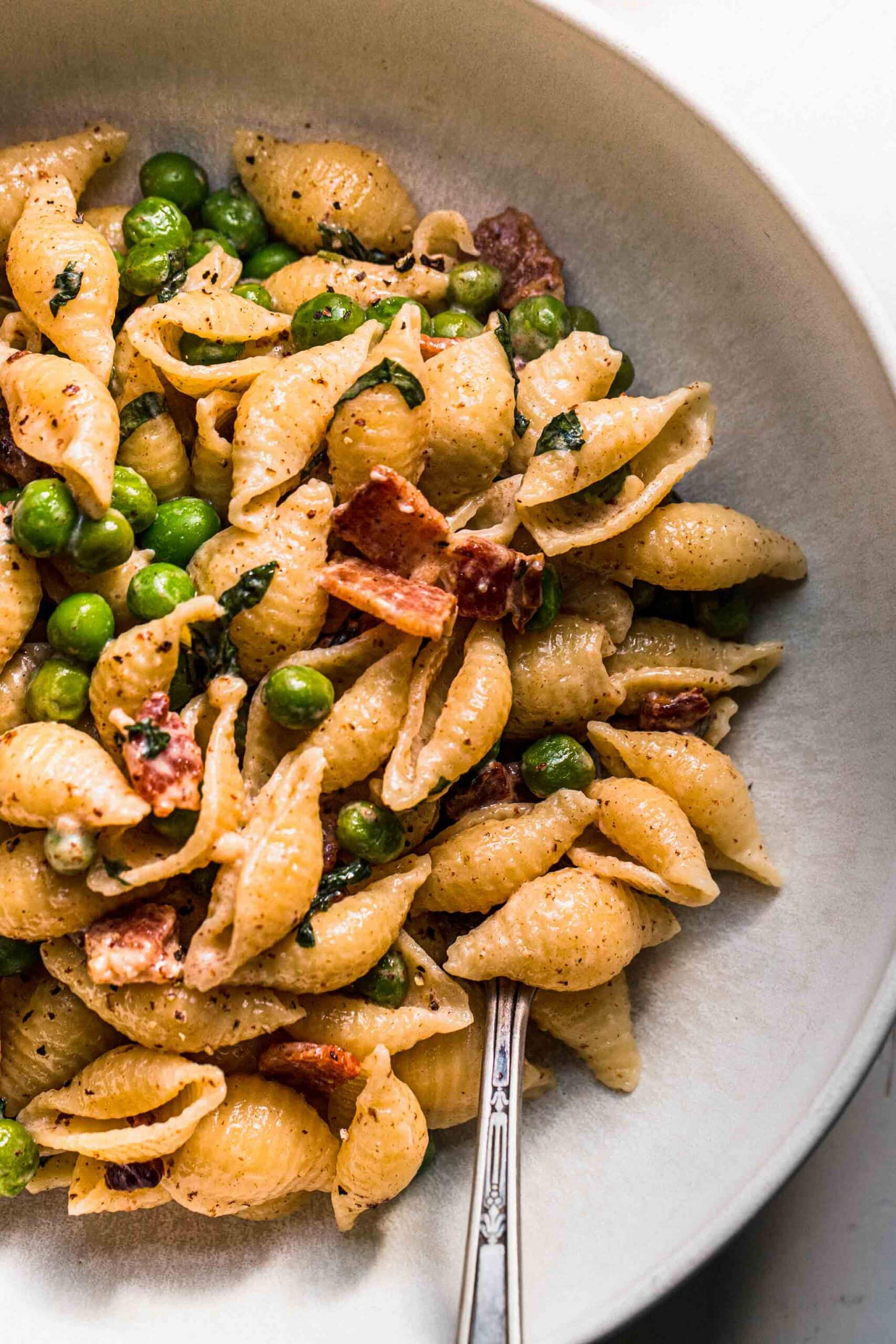 Pasta with peas and bacon in white bowl with fork.
