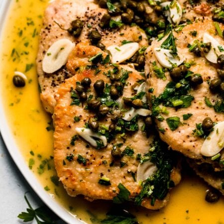 Pork piccata slices on white plate drizzled with lemon caper sauce.