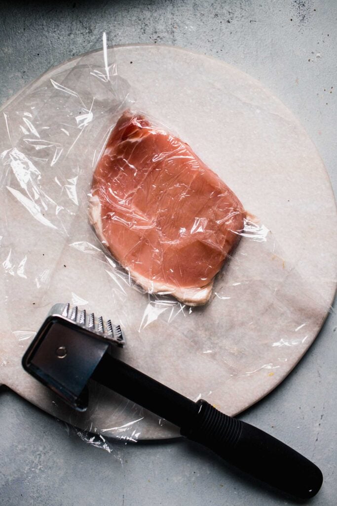 Pork cutlet being flattened with mallet. 