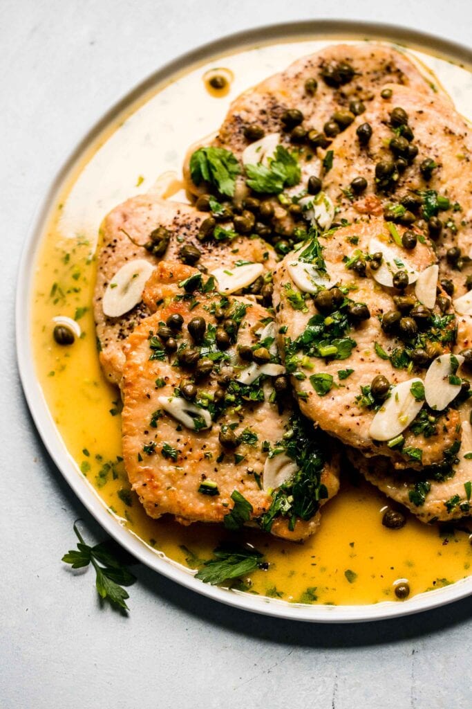 Pork piccata slices on white plate with glossy sauce. 