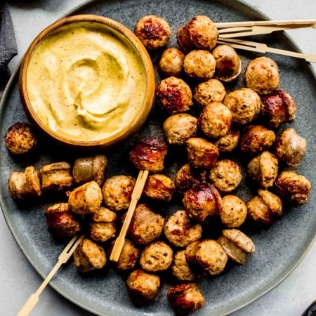 Sausage bites arranged on grey plate with small bowl of mustard sauce.