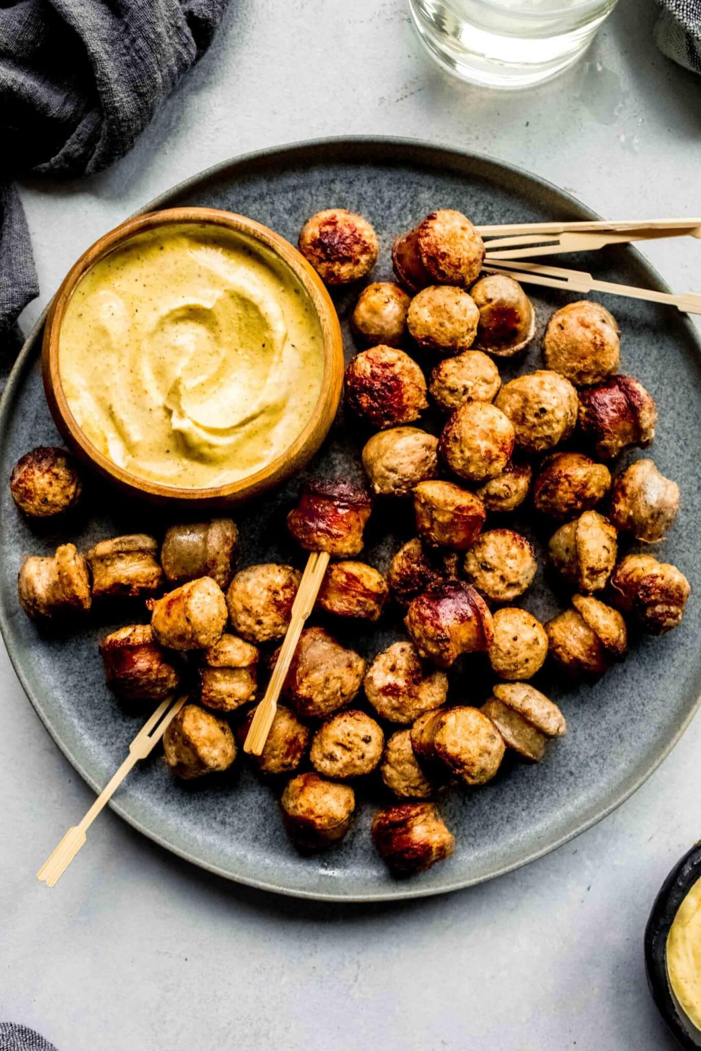 Sausage bites arranged on grey plate with small bowl of mustard sauce.