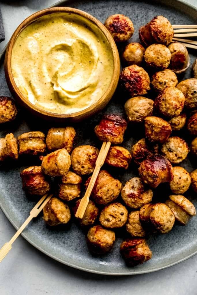 Sausage bites arranged on grey plate with small bowl of mustard sauce.