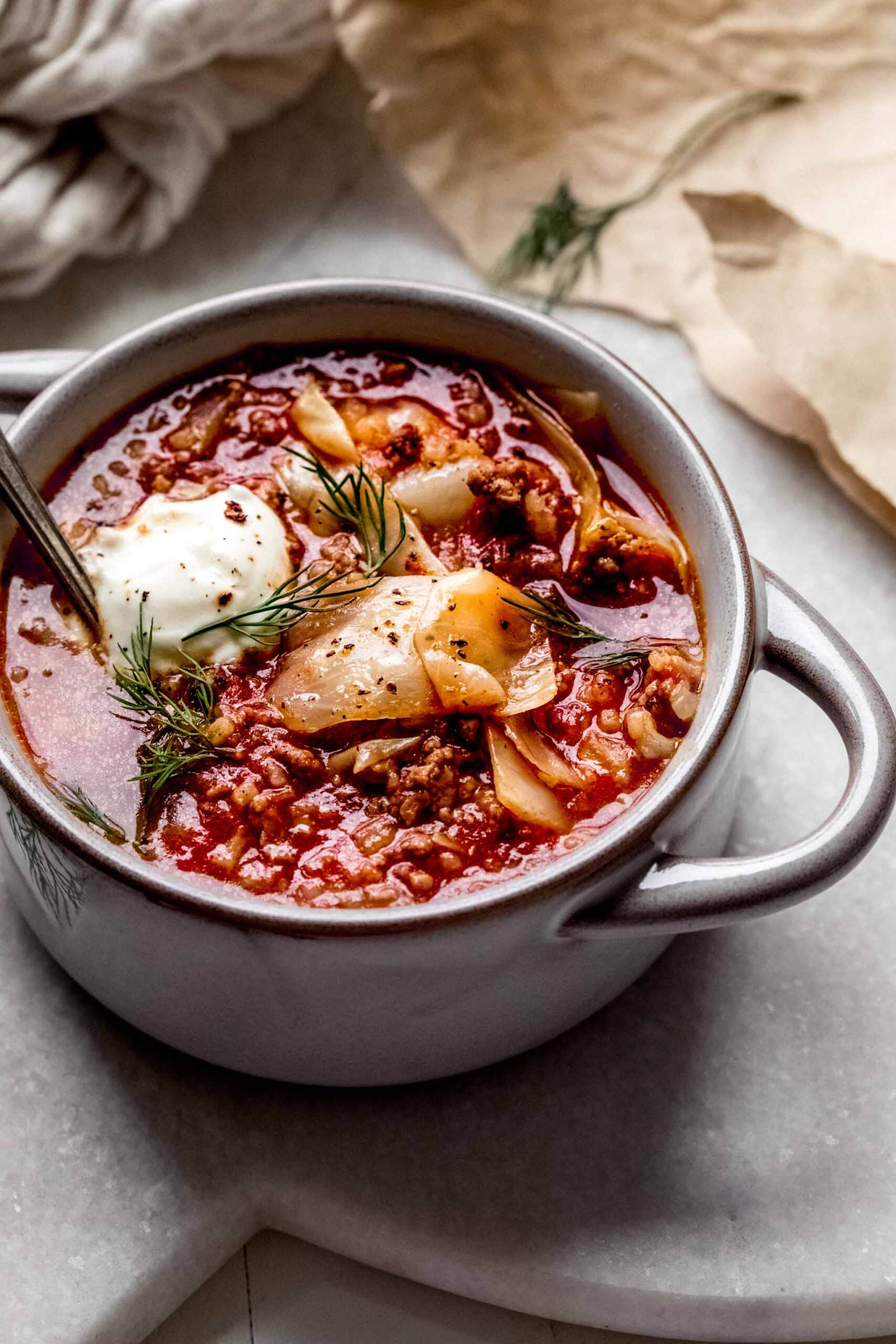 Bowl of cabbage roll soup topped with dollop of sour cream & fresh dill.