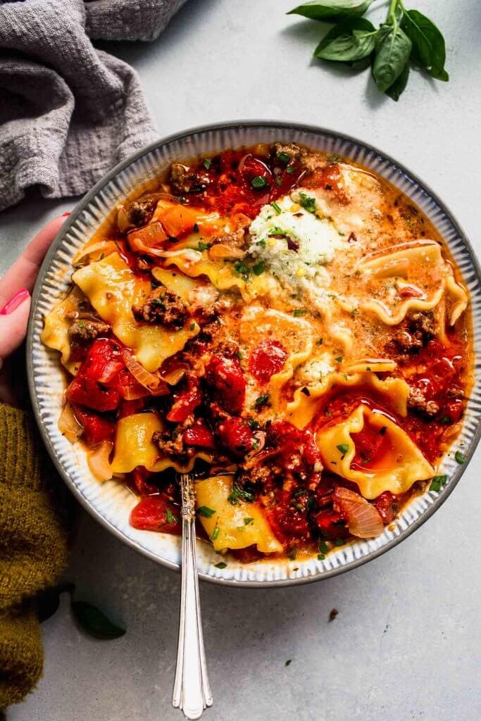 Hand holding bowl of lasagna soup.