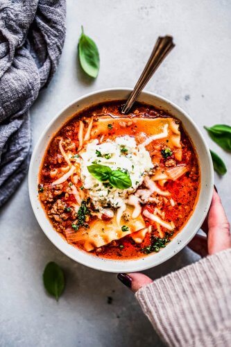 Hand holding bowl of lasagna soup.