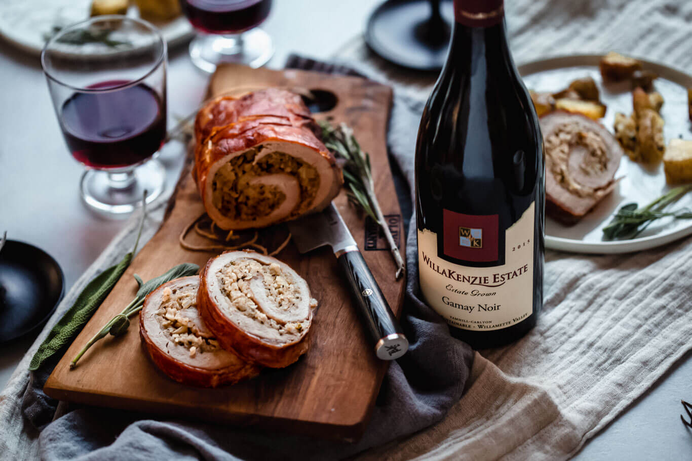 Side view of prepared Prosciutto Wrapped Pork Tenderloin next to bottle of wine.
