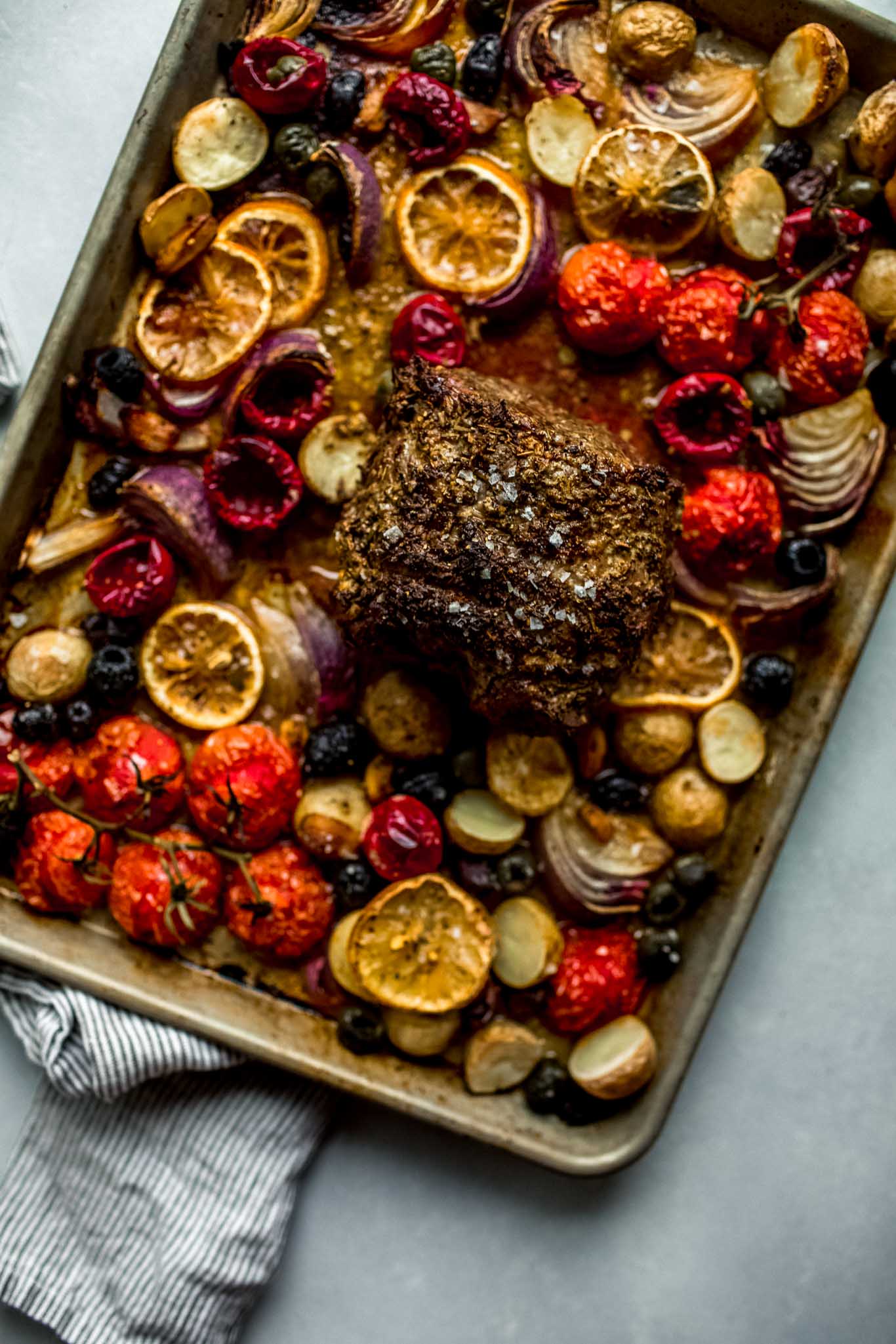 Veggies and olives arranged on sheet pan topped with lamb - out of oven.