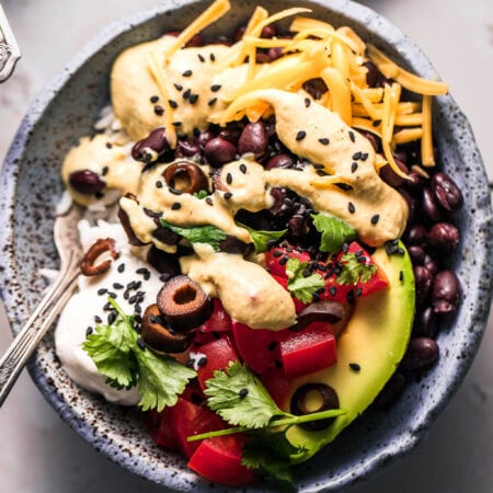 Overhead close up of finished yumm bowl with avocado, tomatoes, black olives cheese cilantro and sour cream.