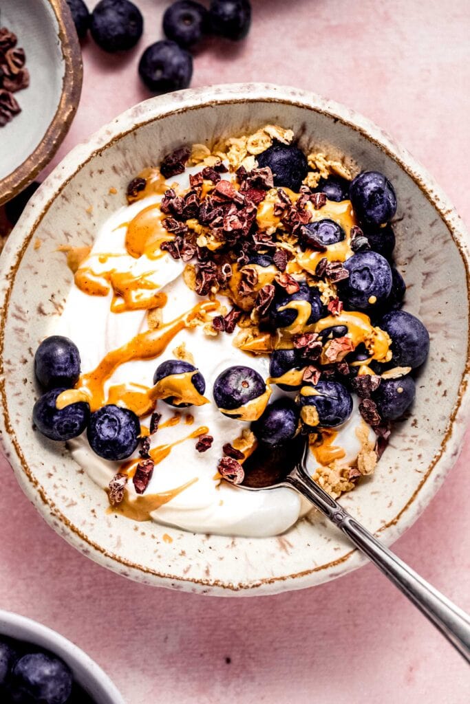 Greek yogurt bowl topped with blueberries, cacao nibs and peanut butter.