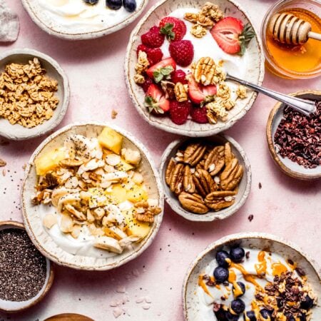 Four different greek yogurt bowls on counter next to small bowls of toppings.