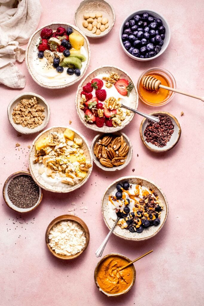 Four different greek yogurt bowls on counter next to small bowls of toppings.
