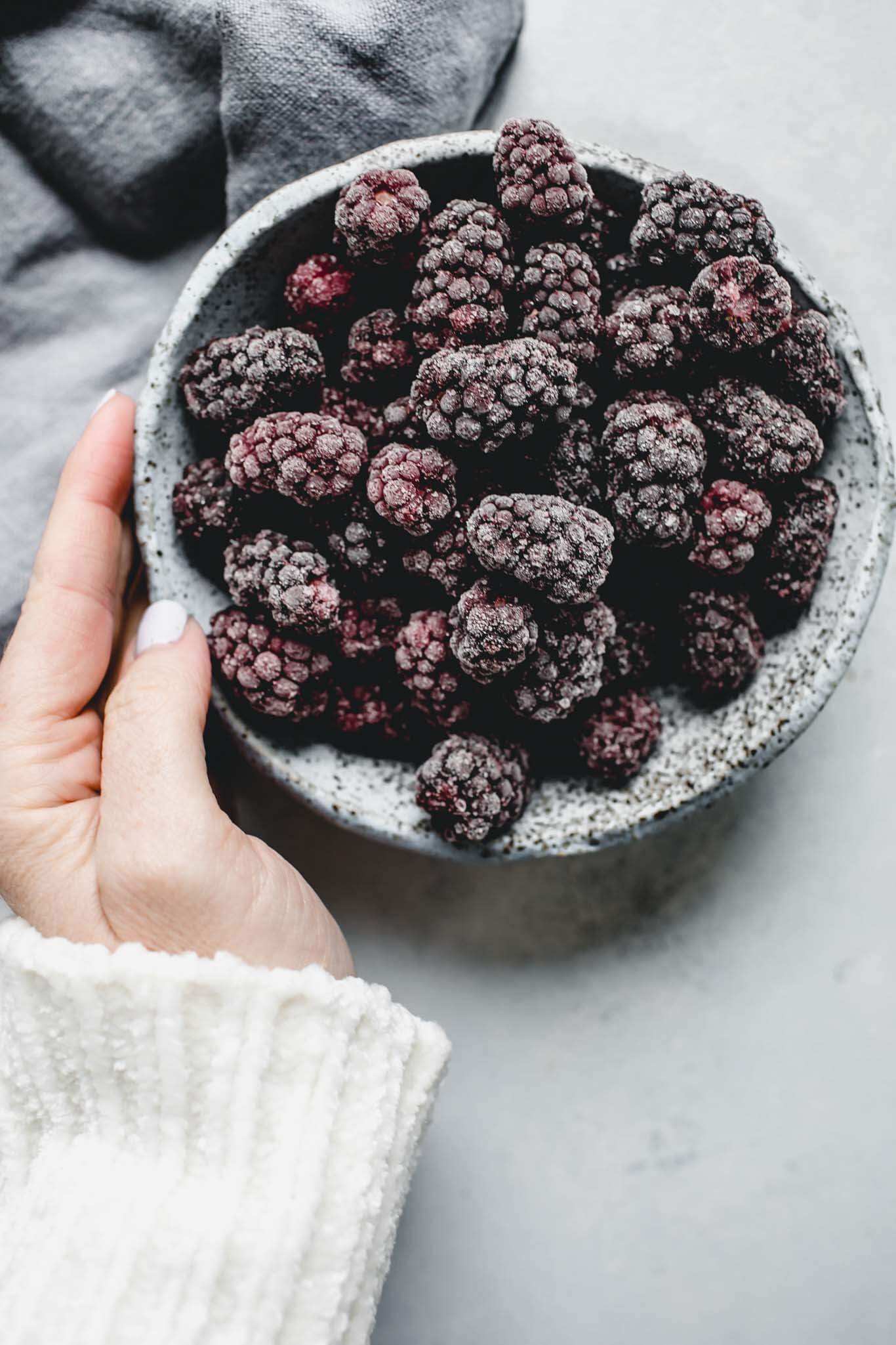 Hand holding bowl of frozen blackberries.
