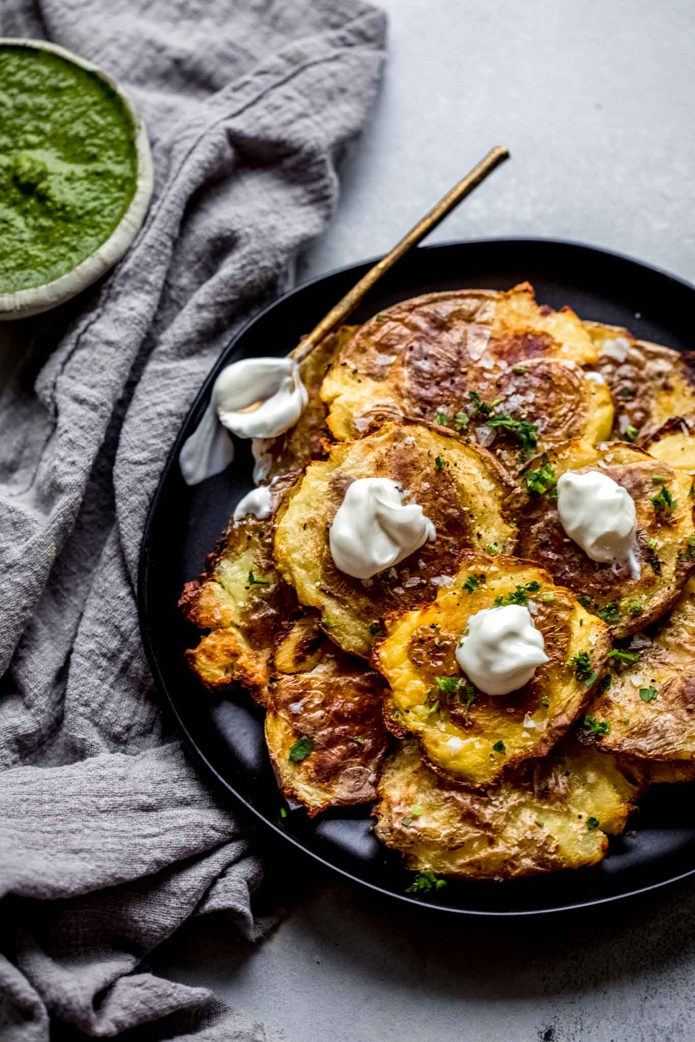 Crispy smashed potatoes on black plate topped with sour cream.