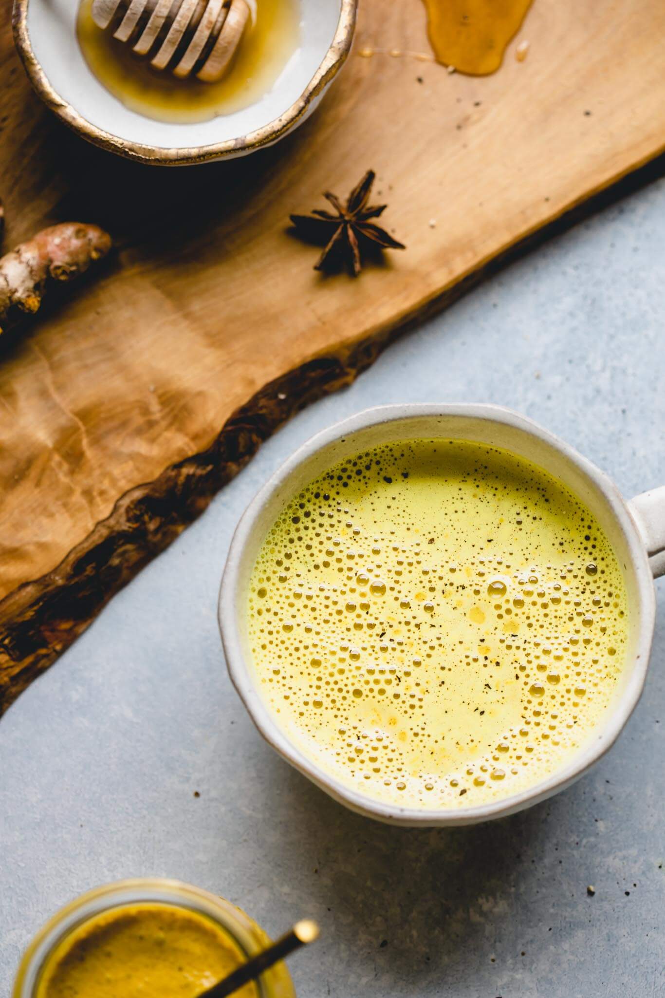 Golden milk latte in mug next to concentrate and honey. 