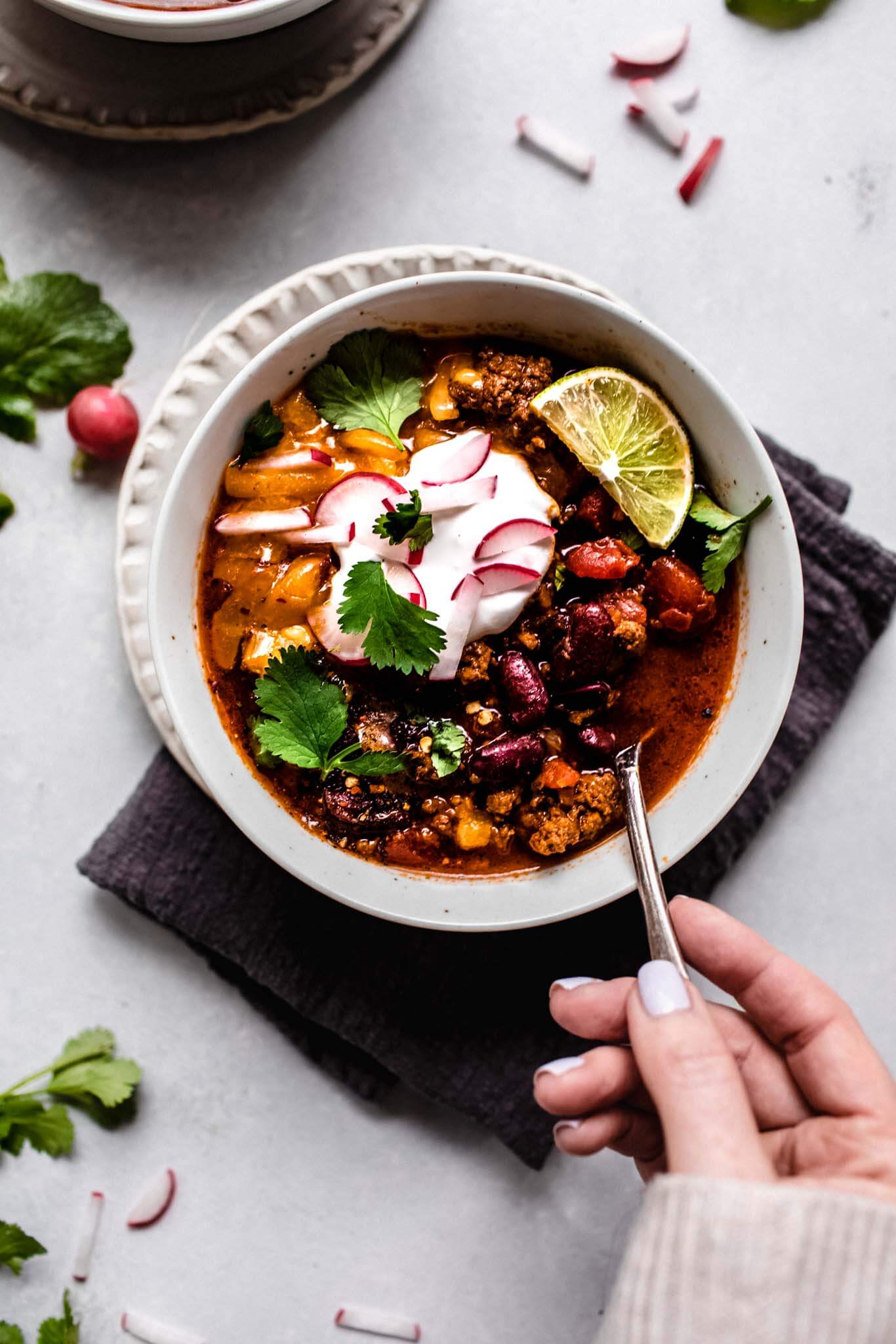 Hand holding spoon in bowl of instant pot chili.