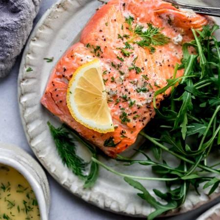 Piece of salmon on plate next to salad.