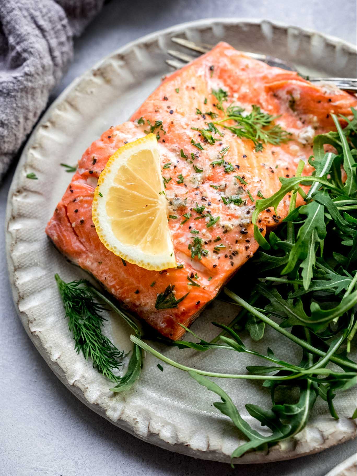 Piece of salmon on plate next to salad.