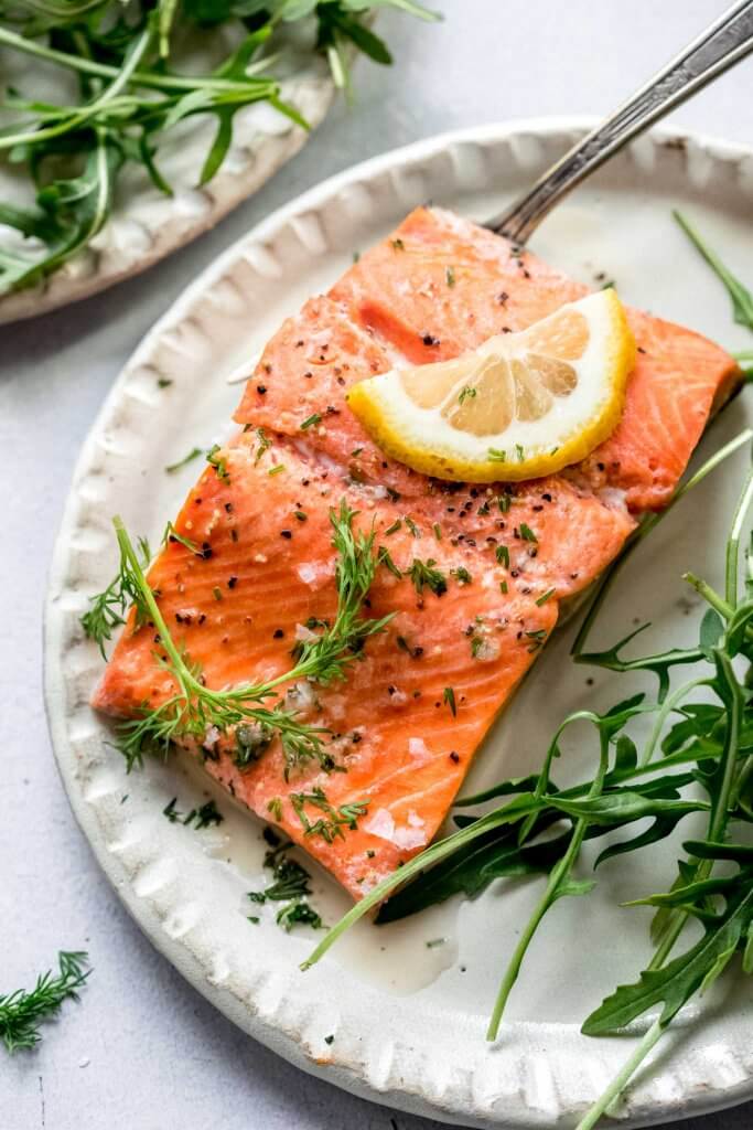 Piece of salmon on plate next to salad.
