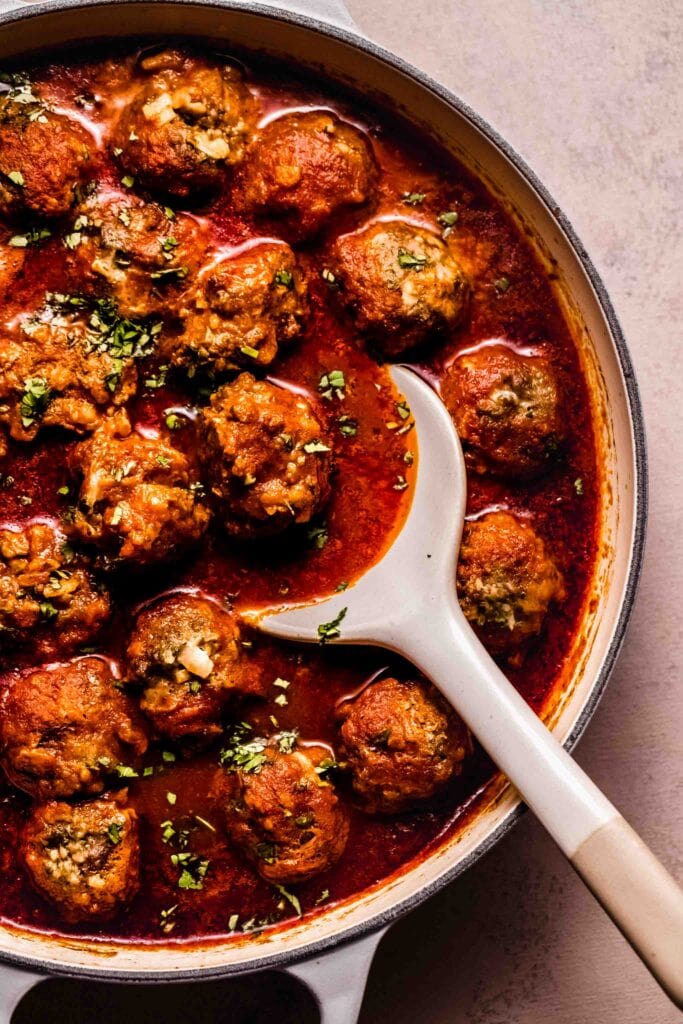 Close up of saucy spanish meatballs in skillet with serving spoon. 