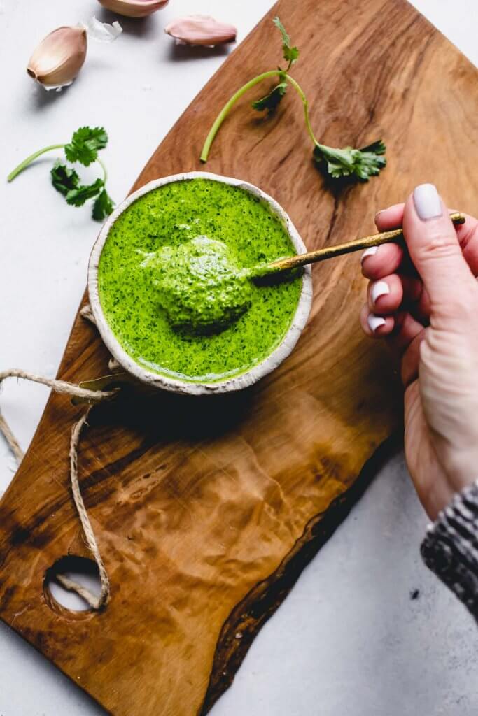 Hand dipping spoon into bowl of mojo sauce. 