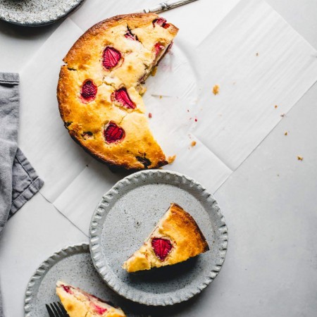 Overhead shot of strawberry ricotta cake cut up with three serving plates of cake.