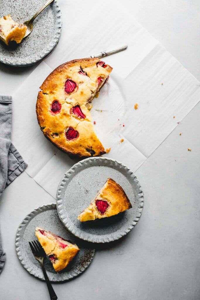 Overhead shot of strawberry ricotta cake cut up with three serving plates of cake.