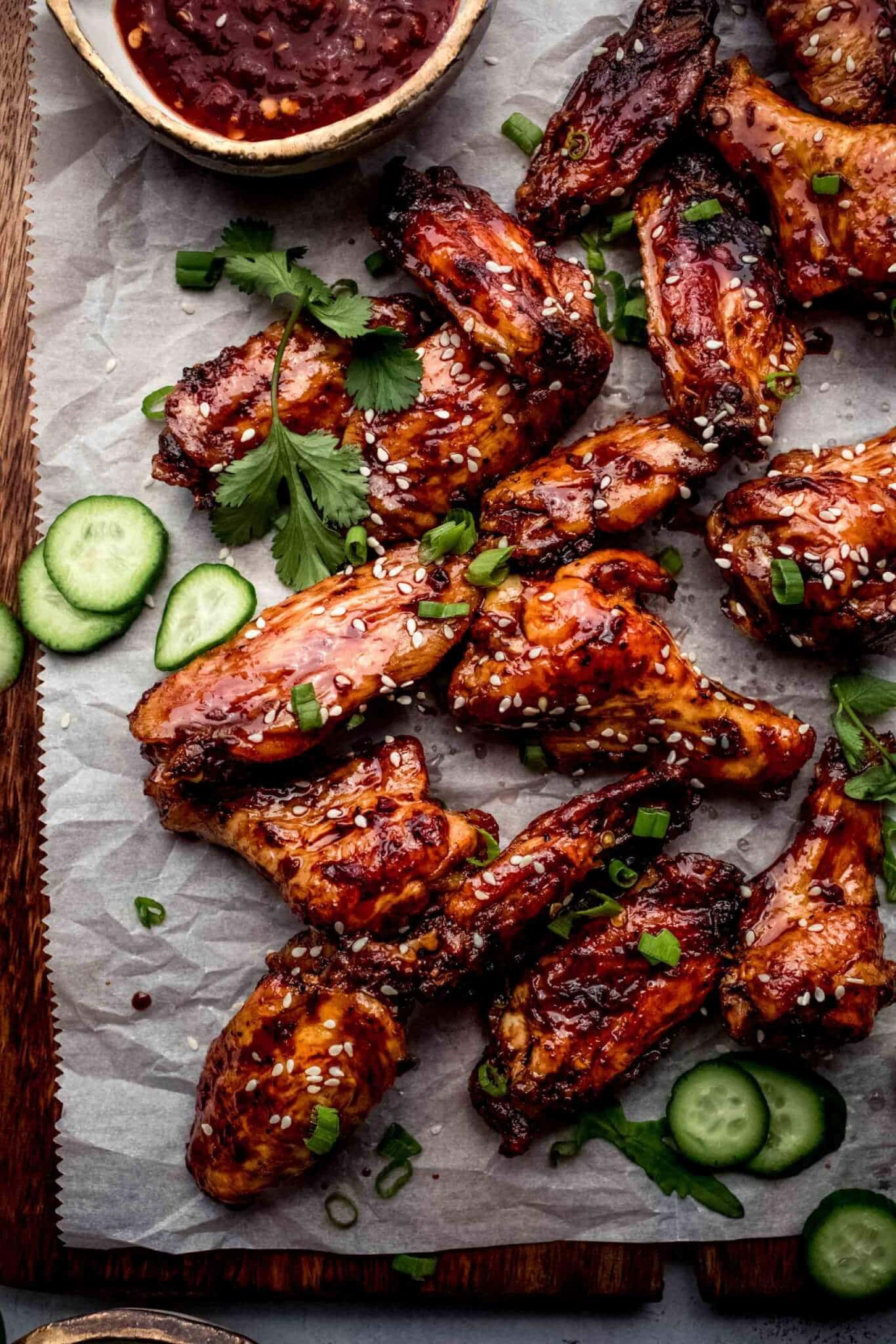 Sticky vietnamese chicken wings on serving platter next to small bowl of hot sauce.