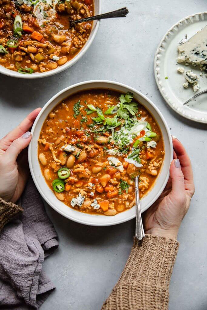 Two hands holding bowl of buffalo chicken chili. 