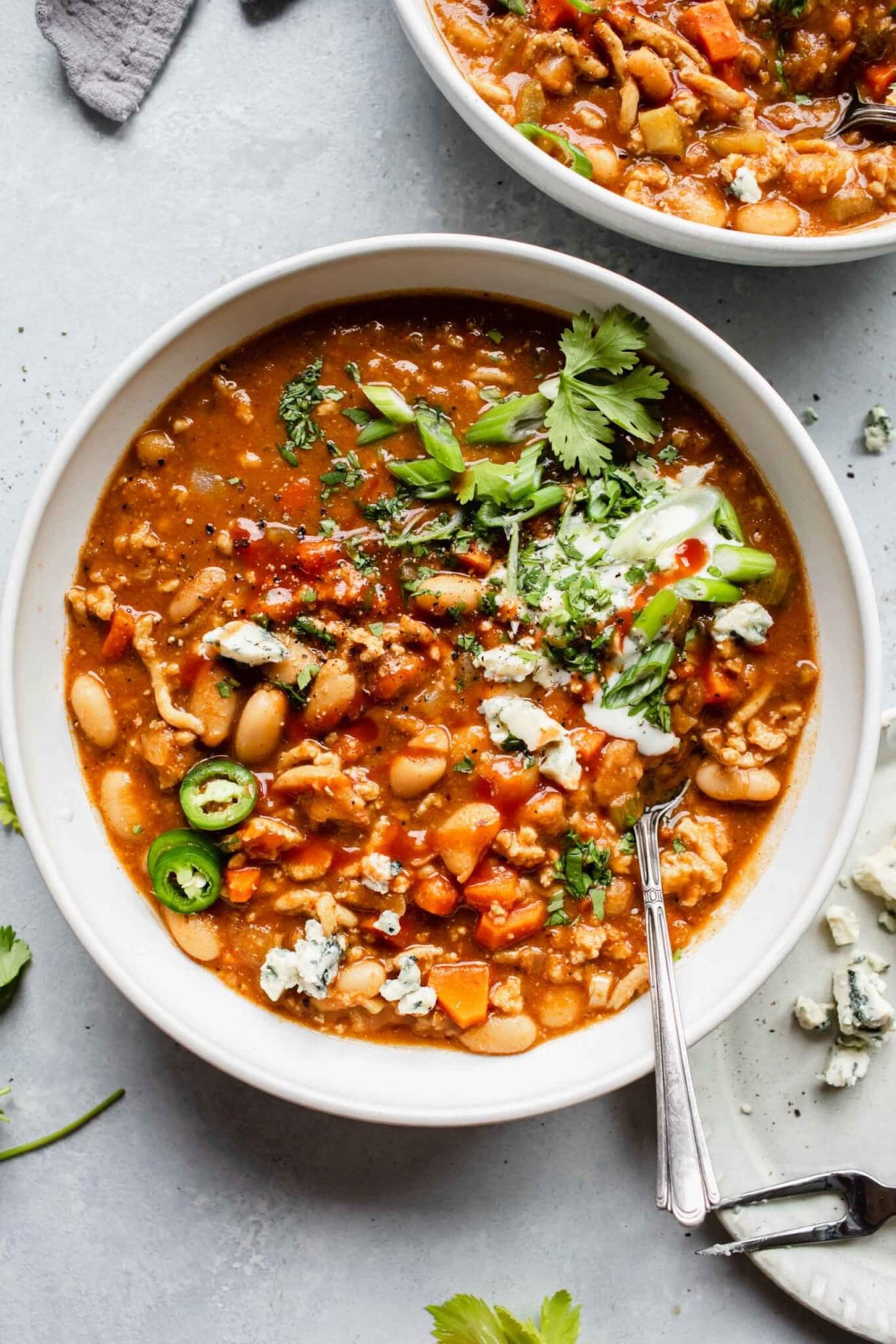 Bowl of buffalo chicken chili topped with blue cheese and celery leaves.