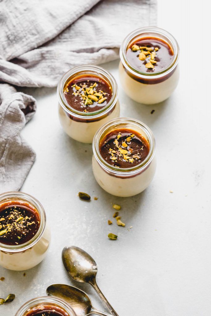 Four jars of butterscotch budino topped with salted caramel and pistachios.